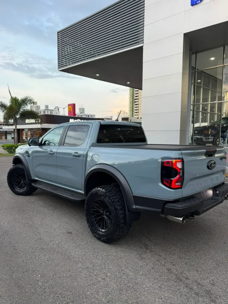Camioneta pick-up Ford Ranger Raptor de color gris con llantas todoterreno frente a un concesionario.
