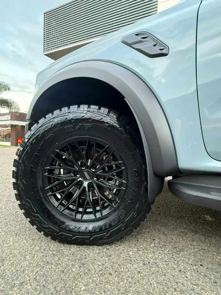 Llanta de aleación negra con neumático de tacos para todoterreno en un vehículo 4x4 azul claro.