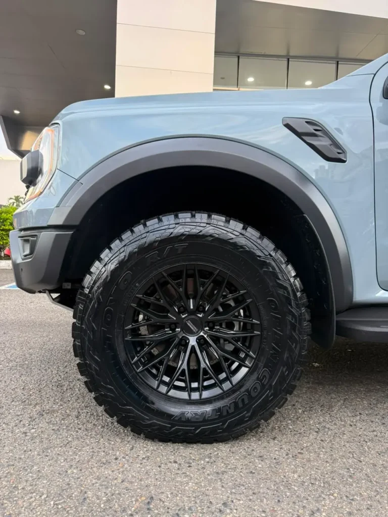 Llanta negra de diseño multirradio con neumático todoterreno en una camioneta gris claro.