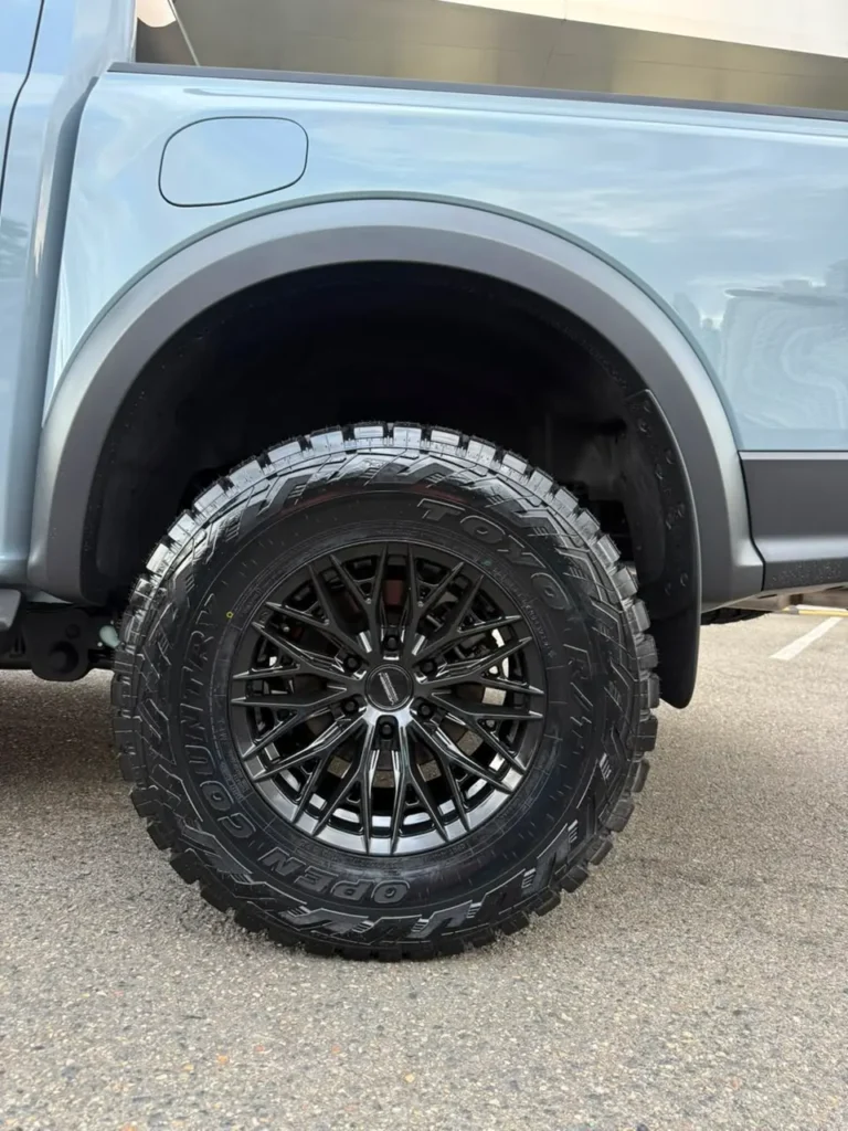 Rueda con neumático todoterreno de gran agarre y llanta de aleación negra en una camioneta pickup gris.