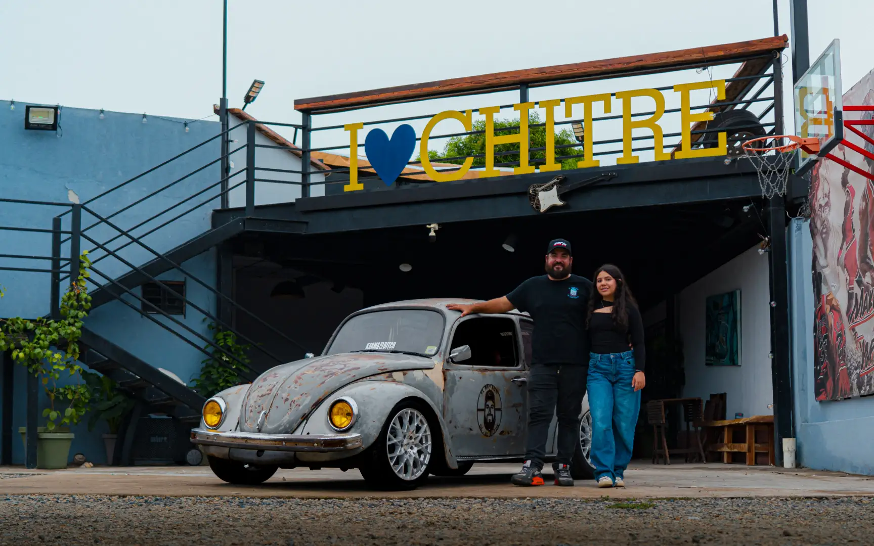 Pareja junto a un Volkswagen Escarabajo clasico con acabado patina frente al letrero de I Love Chitre.