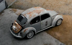 Volkswagen Escarabajo estilo rat rod con carrocería oxidada y rines modernos, visto desde arriba.